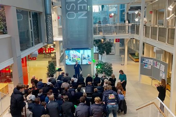 en gruppe mennesker som sitter i et rom med en scene og en stor skjerm